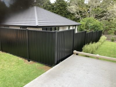 Black corrugated steel privacy fence along a residential side boundary in Whangarei