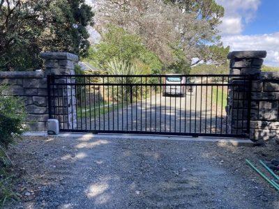 Black metal sliding gate between stone pillars at a rural entrance